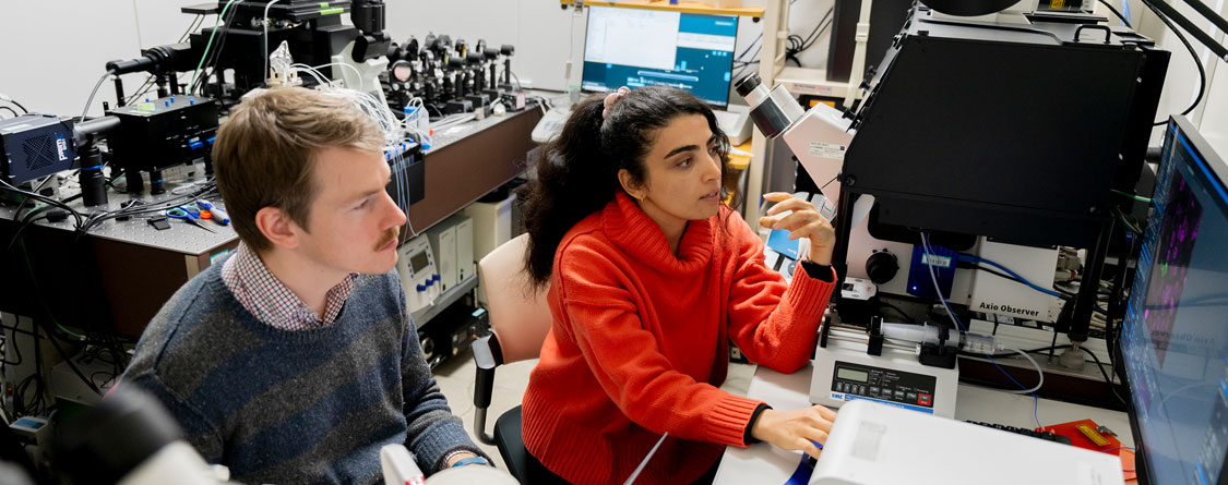 顕微鏡を操作する女性研究者とディスカッションする男性研究者