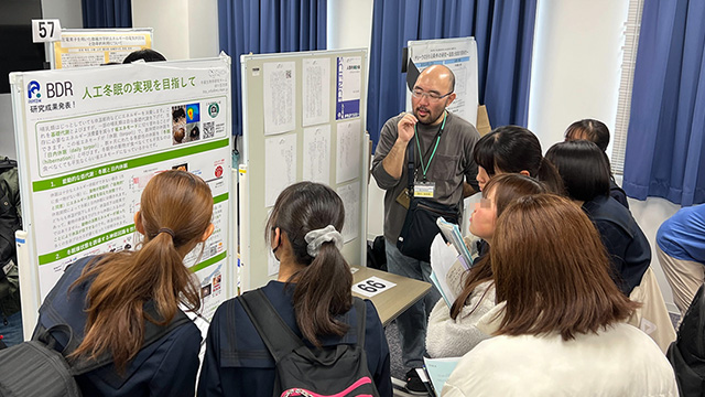 高校生に囲まれ研究成果を説明する研究者